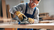 © Tom - Young Caucasian male carpenter in safety goggles and gloves sanding wood, creating a smooth finish in a workshop filled with tools and wood shavings.
