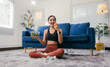 © Parichat - Sitting on a carpet in her living room, a young woman wearing sportswear enjoys a healthy meal of salad and fruit after a fitness workout