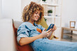 © SHOTPRIME STUDIO - Happy Woman Holding Mobile Phone Relaxing on Sofa in Cozy Living Room