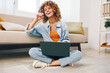 © SHOTPRIME STUDIO - Smiling woman working with laptop in cozy home office, surrounded by modern technology and comfortable living room ambiance.
