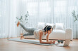 © Monster Ztudio - Young Asian woman in sportswear doing plank on training mat while watching online workout tutorials on laptop in the living room. Sport and recreation concept