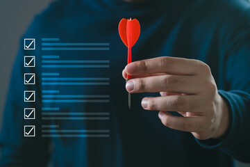 Close-up of a hand holding a red dart, representing focus and precision in decision-making with a checklist.