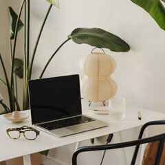 Wall Mural - elegant white desk with laptop, glasses, and unique lamp surrounded by vibrant green plants for offi
