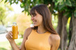 © luismolinero - Young woman holding an orange juice at outdoors with happy expression