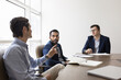 © fizkes - Multiethnic group of three serious young businessmen discussing work project, teamwork, management at conference table, talking in meeting room. Diverse board of directors, team of managers shot