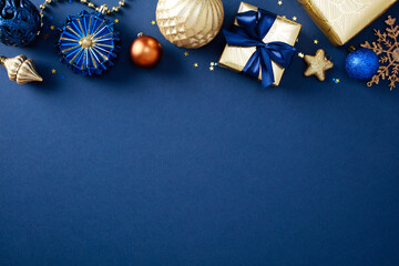 Wall Mural - Frame border of stylish Christmas decorations and gold gifts on blue background. Xmas greeting card design, New Year party invitation template. Flat lay, top view, copy space