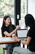 © Satori Studio - Two young women discussing business strategies with charts and laptops in a modern office setting.