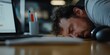© Archil - An exhausted office worker naps at a desk amidst work clutter, bathed in soft lighting.