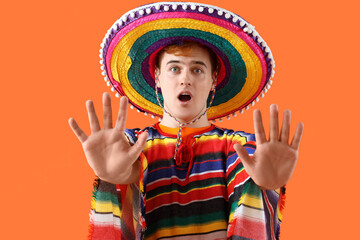 Wall Mural - Scared young Mexican man in sombrero and poncho on orange background