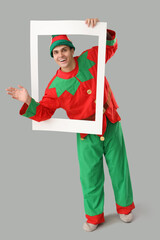 Sticker - Handsome young man in elf's costume with frame waving hand on grey background