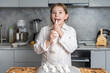 © Andy Shell - Cute little girl in the kitchen cooking meringue in a white jacket, she licks the cream