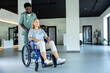 © zinkevych - African american doctor carrying a wheel-chair with a female patient