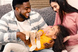 © Prostock-studio - Happy family at home. African american father and white mother tickling daughter