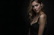 © Nadiya - Portrait of a beautiful smiling young woman with long curly hair and a mysterious look on a dark background in a black evening dress