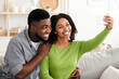 © Prostock-studio - Quarantine Selfie. Smiling black couple taking photo on smartphone at home, capturing happy moments, enjoying spending time together, free space