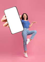 Wall Mural - Check out this new mobile application. Excited young Asian lady jumping, shouting OMG, presenting smartphone with empty screen over pink studio background, mockup for website or app