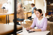 © JackF - Portrait of focused young female freelancer surfing Internet on notebook while drinking tea or coffee in cafeteria