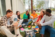 © Jose Calsina - diverse group of happy university students sitting together on green campus lawn while studying reading and discussing with notebooks laptop and backpack during outdoor learning session