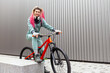 © Богдан Маліцький - young hipster girl with dreadlocks in warm clothes stands with bicycle against gray wall and smiles, female cyclist rides bicycle in cold weather in autumn