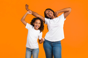 Wall Mural - Having Fun. Portrait of excited young black mother and daughter dancing and fooling around. Happy African American woman and girl enjoying favorite music together on yellow studio background