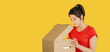 © golubovy - Surprise delivery. Curious woman in red opening cardboard box isolated isolated on yellow empty space background.