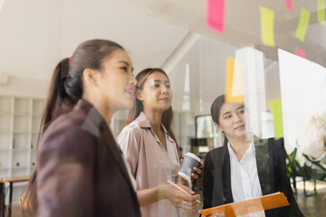 Wall Mural - Asian businesswoman teamwork planning with sticky notes and new ideas on a glass wall, Business people brainstorming strategy and new ideas concept, startup worker meeting,