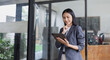 © SOMKID - Asian businesswoman holding tablet standing in office.