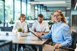 © ty - Attractive young businesswoman sitting on the table, looking at camera with colleagues on the background