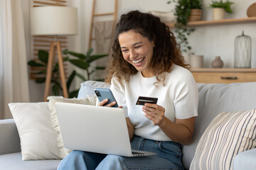 Wall Mural - Happy woman using a credit card and mobile phone for online shopping at home