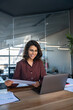 © Stock 4 You - Smiling latin hispanic young business woman working on laptop computer reading financial document report in office. Accountant entrepreneur manager businesswoman doing paperwork using pc. Vertical