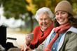 © Halfpoint - Portrait of a granddaughter and grandmother sitting on bench in autumn park, drinking coffee and talking.