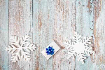 White decorative snowflakes and giftbox on white wooden background, copy space