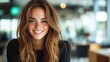 © JoxyAimages - A young woman with long hair and freckles smiles warmly, set against a blurred modern office backdrop, conveying friendliness and approachability.