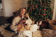 © polinaloves - Young beautiful woman and her cute dog sitting under Christmas tree in a decorated living room.