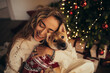 © polinaloves - Young beautiful woman and her cute dog sitting under Christmas tree in a decorated living room.