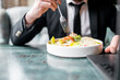 © pavel siamionov - Close-up of a person dining in a restaurant, focusing on their hand using a fork to eat a salad with shrimp and avocado, conveying the concept of healthy eating or dining out.