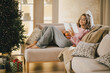 © polinaloves - Young woman relaxing, reading book and drinking cocoa in a cozy living room near Christmas tree.