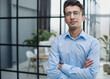 © Katsiaryna - Confident sincere young businessman stands in the office with his hands crossed