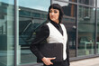 © Iryna - Young businesswoman in a vest holds a briefcase while standing confidently outside an office building on a sunny day