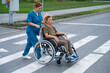 © Михаил Решетников - Red-haired nurse pushing an elderly woman in a wheelchair across the road.