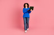 © deagreez - Young woman with curly hair and vibrant casual outfit holding laptop against pink background, ideal for business and technology themes