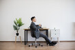 © sofiko14 - Asian male adult businessman sitting in modern office enjoying coffee break. He leans back on swivel chair while holding beverage, laptop open on desk, against minimalistic white wall background.