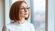 © Nut S. - Beautiful 45 years old gentle ginger red hair caucasian woman wearing glasses looking out the window. She is wearing a white shirt.