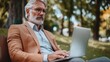 © michnik101 - Older man working on laptop outdoors in a park, serene natural environment