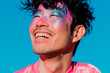 © Katie R - happy queer asian man with glitter on his face wearing pink t-shirt