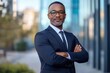 © SerPak - An African man in his forties stands confidently against the backdrop of a sleek business center. He wears a stylish suit and cool shades, embodying professionalism and modern elegance in his relaxed