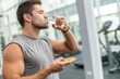 © SerPak - A young man with a fit physique stands in a contemporary gym, casually taking dietary supplements with a glass of water. The atmosphere is bright, reflecting the commitment to health and fitness durin