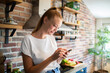 © Geber86 - Young woman holding smartphone in modern kitchen