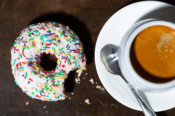 Wall Mural - sweet donut with white frosting and cup of coffee on wooden background, top view closeup