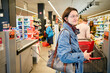 © Connect Images - Woman with glasses and a denim jacket pushing a shopping cart in a grocery store aisle.